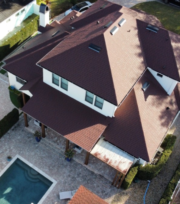 Aerial view of a white house with a new red shingle roof installed by Nine Square Roofing